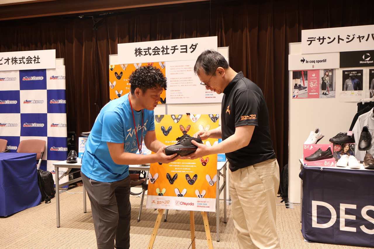 河合純一スポーツ庁長官が株式会社チヨダのブースでオリジナルシューズについて解説を受けている画像